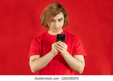 Young Man Prep Student With Long Hair. 20s Guy With Smartphone On A Red Background.