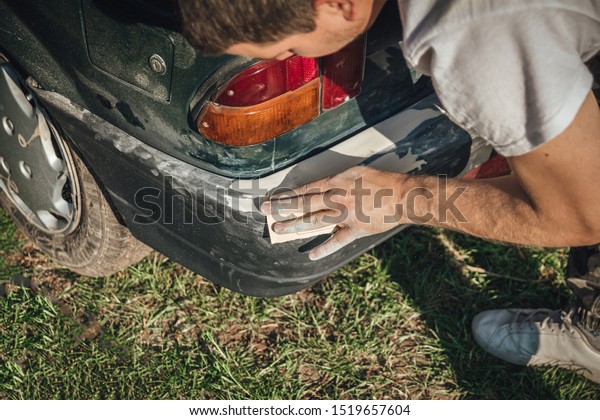 Young man prepairing car\
for painting. Using sandpaper to repair bumper. Old timer and small\
business.