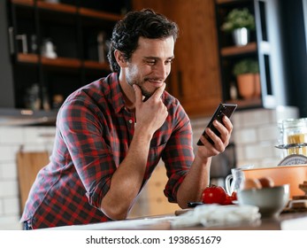 Young Man Preparing Breakfast And Using The Phone. Man Reading News Online In The Morning.	