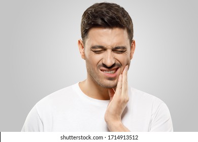 Young man pressing fingers to his jaw, trying to overcome severe toothache, eyes closed, isolated on gray background