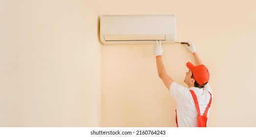 Young man professional technician in red overall fixing the AC air conditioning with screwdriver. Copy space for your text - Shutterstock ID 2160764243