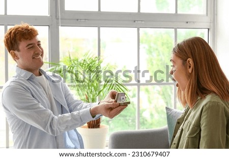 Young man proposing to his shocked girlfriend at home