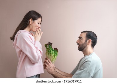 Young man proposing to woman with bunch of salad leaves, healthy eating choice. Funny shot, humor concept, studio portrait, close up. Copy space for text