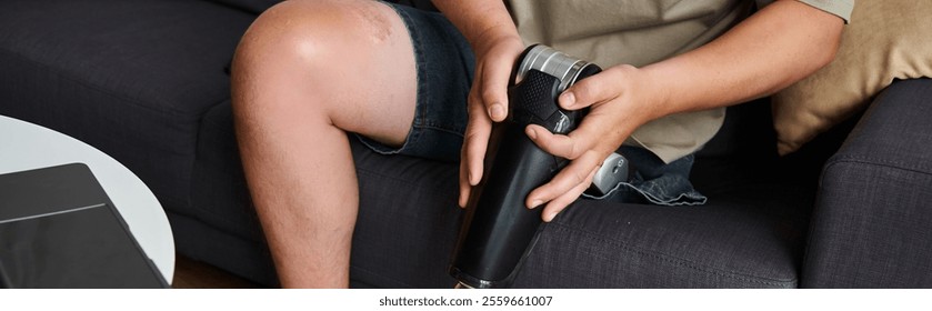 A young man with a prosthetic leg sits on a couch, adjusting the device with focused attention. - Powered by Shutterstock