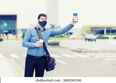 Young Man With Protective Face Mask Using Mobile Phone App Waiting For Rideshare – Casual Business Man With Hand Up Calling Taxi Hailing From Sidewalk – Passenger Using Online Map To Call Cab