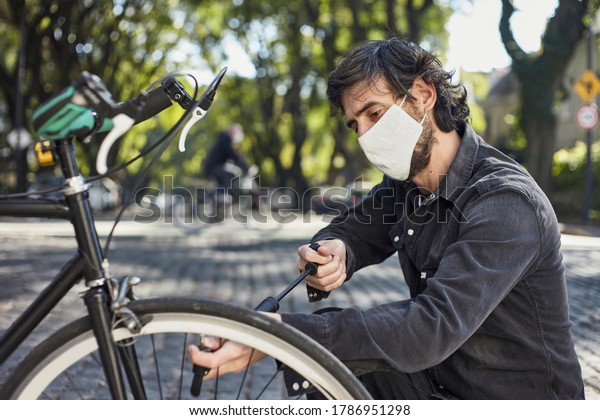 Young man with protective mask against covid\
inflates the wheel of his\
bicycle.