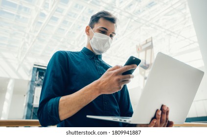 young man in a protective mask is choosing a contact in his smartphone