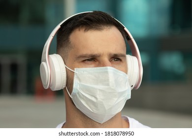 Young Man In Protective Medical Face Mask Listen Music With Wireless Bluetooth Earphones. COVID-19 Coronavirus.