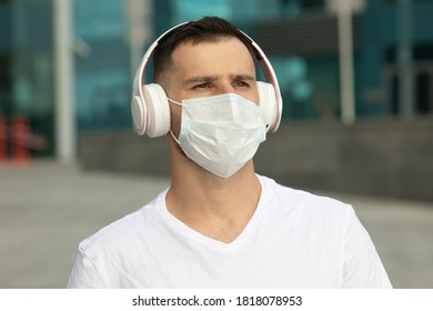 Young Man In Protective Medical Face Mask Listen Music With Wireless Bluetooth Earphones. COVID-19 Coronavirus.