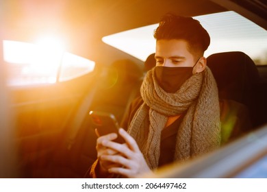 Young Man In Protective Sterile Mask In Taxi Car On A Back Seat  Checking Her Cell Phone. Safety And Pandemic Concept. Work On The Way To The Office. Covid-2019.