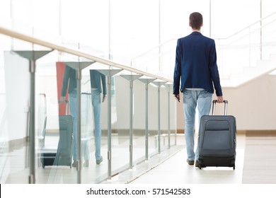 Young man pulling suitcase in modern airport terminal. Travelling guy or businessman concept. Business trip