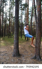 a young man pulls himself up on one arm on a horizontal bar in the woods