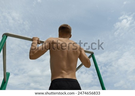 Young man pulls himself up on horizontal bar on sports field outdoors