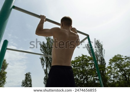Young man pulls himself up on horizontal bar on sports field outdoors