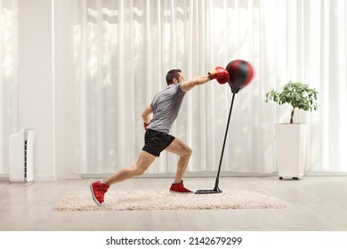 Young Man Punching A Free Standing Boxing Bag At Home