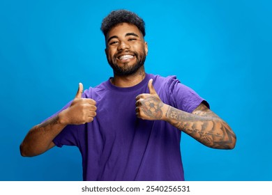 Young man in purple shirt stand against blue background, giving double thumbs-up with big smile, showing his positive and confident attitude. Concept of human emotions, youth, social media. - Powered by Shutterstock