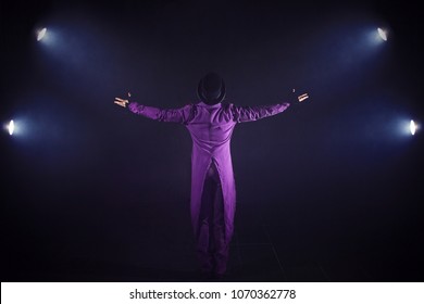 Young man in purple suit standing on the background of the spotlight. Showman spreading hands, show begins. Back view - Shutterstock ID 1070362778