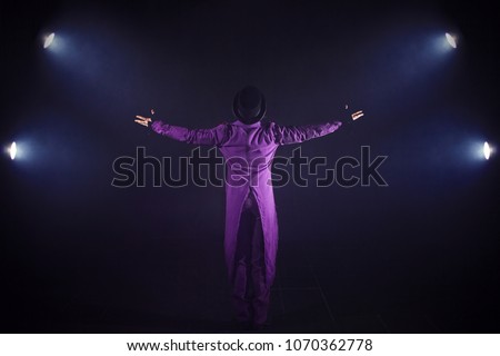 Young man in purple suit standing on the background of the spotlight. Showman spreading hands, show begins. Back view