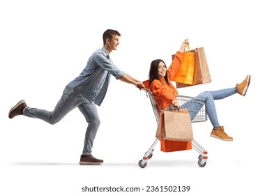 Young man pushing a female with shopping bags inside a shopping cart isolated on white background