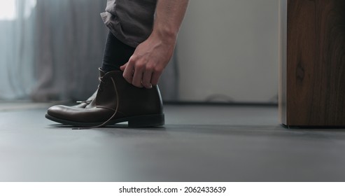 Young man put on his brown leather chukka boots indoor