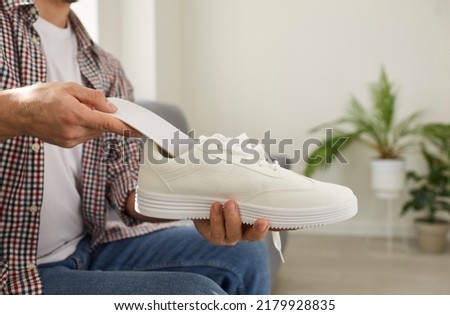 Young man puts new clean orthotic insole with foot arch support inside modern white comfortable orthopedic shoe he is holding in his hand. Cropped shot. Pain treatment and flatfoot prevention concept