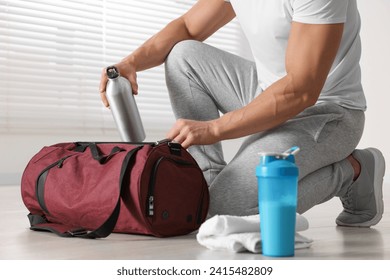 Young man putting bottle of water into bag indoors, closeup. Shaker with protein and towel on floor - Powered by Shutterstock