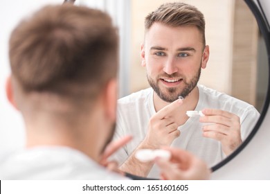 Young man putting in contact lenses near mirror - Powered by Shutterstock