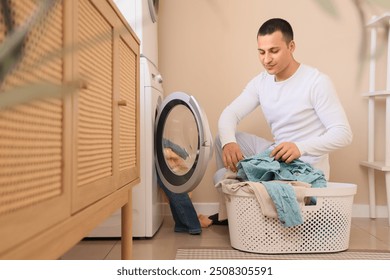 Young man putting dirty clothes into washing machine in laundry room - Powered by Shutterstock