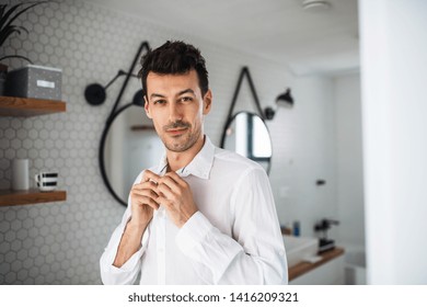 Young Man Putting On Shirt In The Bathroom In The Morning.