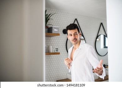 Young Man Putting On Shirt In The Bathroom In The Morning.