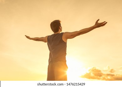 Young man raising his arms up to the sky against the sunset feeling free.  Happiness, freedom, and joy concept. 