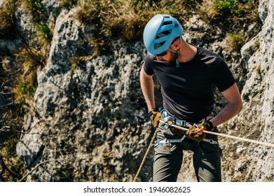 Young man rappelling down a rocky cliff, he is attached on rope with a figure eight and carabiner. Extreme adventure in the mountains.