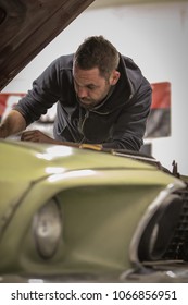 A Young Man Is Reaching Under The Hood Of An Old Vintage Car Fixing The Engine. Man Struggling To Fix The Engine Of A Green Muscle Car.