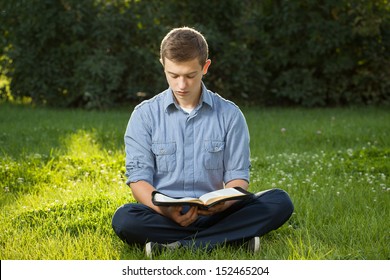 Young Man Reading Bible In A Park