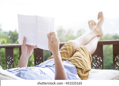 Young Man Reading A Book Lying On Soft Mattress In Relaxing Bed At Terrace With Green Nature View. Fresh Air In The Morning Of Weekend Or Free Day. Relax Or Education Background Idea. Selective Focus.