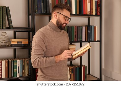 Young Man Reading Book Near Shelves In Home Library