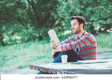 Young Man Reading A Book In The Park