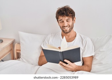 Young man reading book sitting on bed at bedroom - Powered by Shutterstock