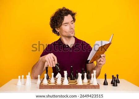 Young man reading a book while playing chess, contemplating strategy against a bright yellow background
