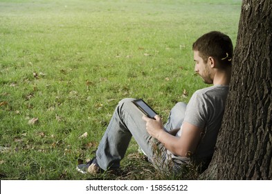 	Young man reading e-book under the tree