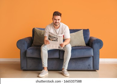 Young Man Reading Newspaper While Sitting On Sofa At Home