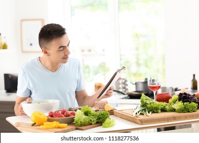 Young Man Reading Recipe Book In Kitchen