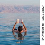 Young man reads a book floating in the waters of the Dead Sea in Israel
