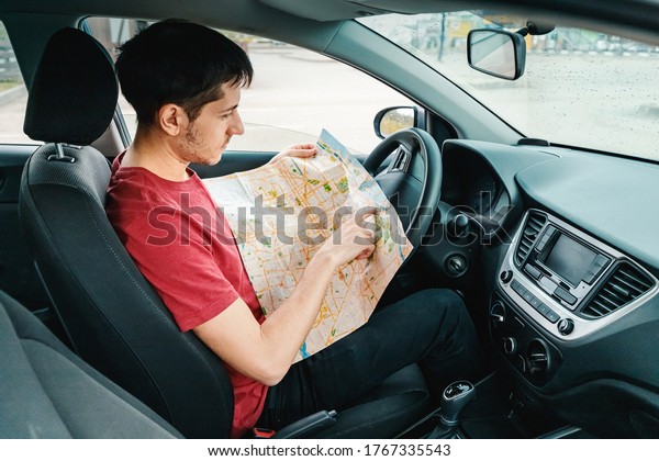young man reads the map and looks\
for the destination driving his car. Travel and trip\
concept