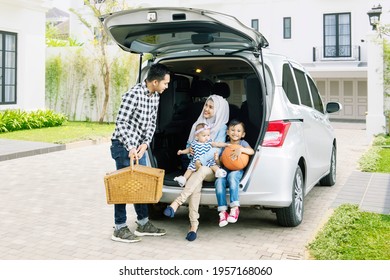 Young Man Ready For Vacation With His Family While Holding A Picnic Basket Into The Car Trunk. Shot In The Front Of House