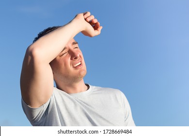 Young Man Received Sun And Heat Stroke And Headache. Guy Holds His Head In His Hands And Protects Himself From The Sun Outdoors Against Background A Blue Sky