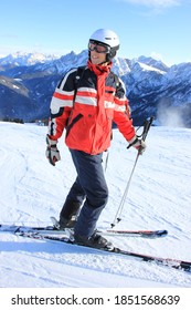 Young Man In Red Black Ski Outfit And Helmet, In Front Of Blue Sky And Mountain Background And Snowy Ground, Skiing On The Dolomite Ski Paradise 