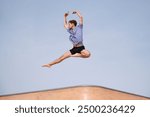 Young man with red hair is gracefully leaping through the air in front of a blue sky