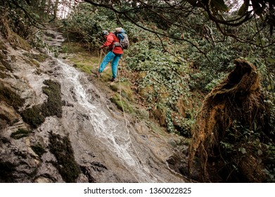 Young man in red jacket with backpack dulfers down the mountains near waterfall in Adjara