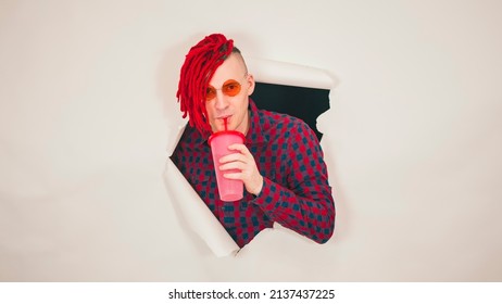 Young man in red plaid shirt drinking through soft drink straw in hole of white background. Bright guy enjoying nonalcoholic beverage - Shutterstock ID 2137437225